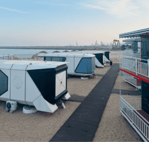 บ้านสำเร็จรูปสไตล์โมเดิร์น - กระท่อมริมชายหาดสำเร็จรูปล้ำยุคที่มีการออกแบบทางเรขาคณิต ตั้งอยู่บนชายหาดทรายพร้อมทางเดิน