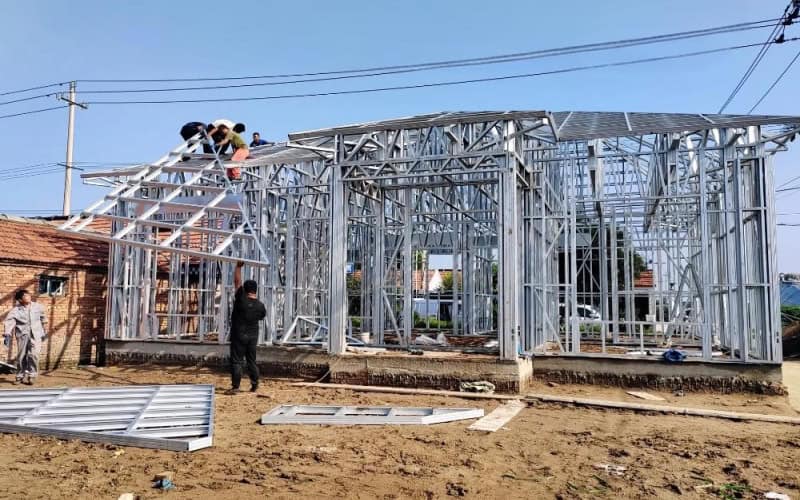 Steel - framed structure under construction on a dirt site, with metal components laid out.