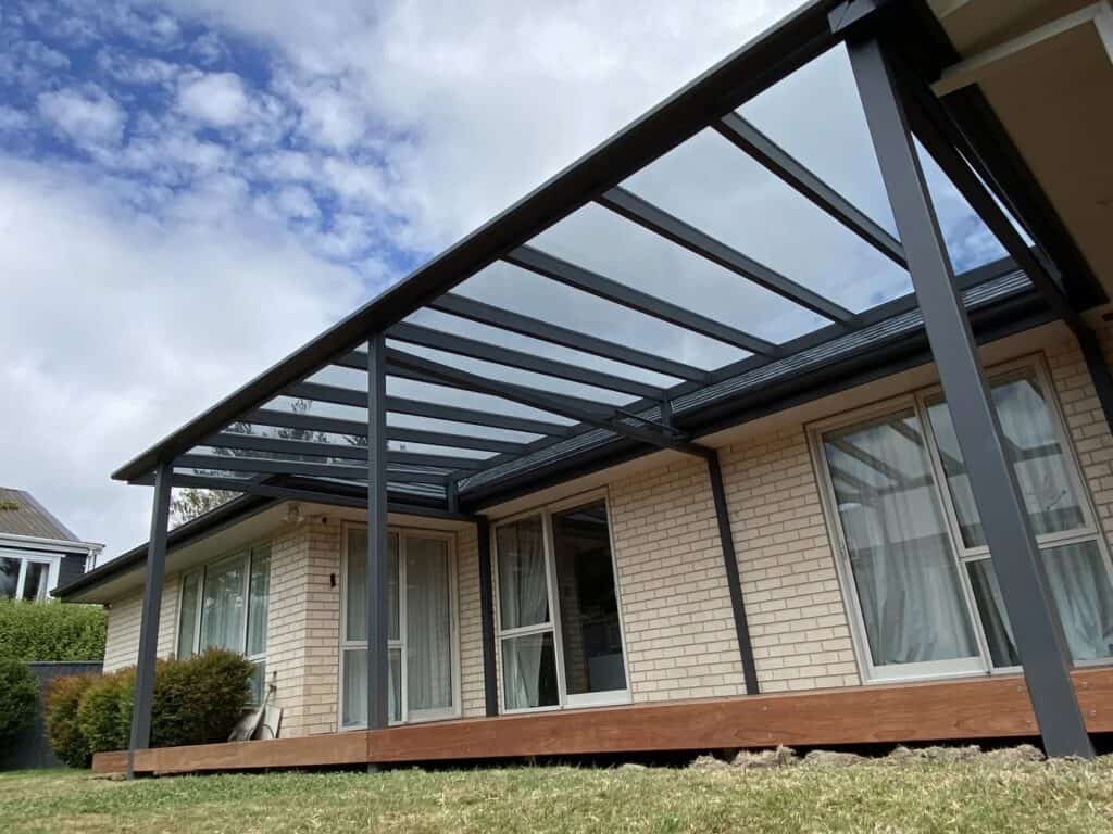 House with a prefabricated glass - and - metal patio cover, wooden deck below.