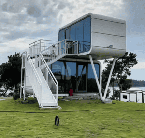 Ein modernes, erhöhtes Fertighaus mit einzigartigem Design, großen Glasfenstern, einer Treppe, die zum Eingang hinaufführt, und einer malerischen Landschaft im Hintergrund.