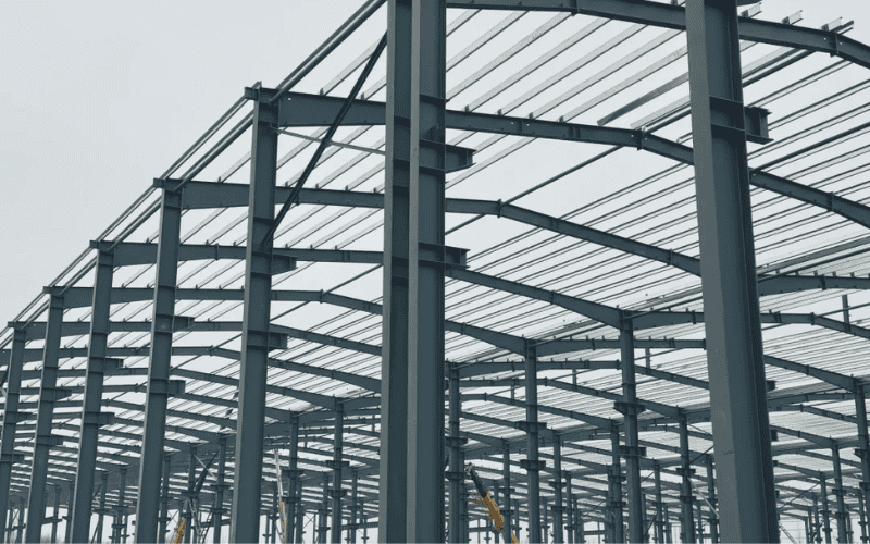 Close-up view of a large steel building framework, highlighting vertical columns and horizontal beams in a spacious industrial layout.