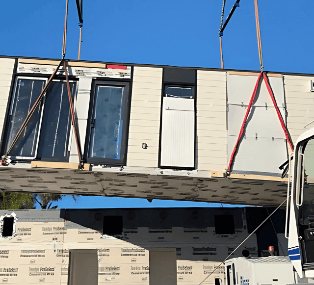 A prefabricated building module being lifted by a crane for assembly at a construction site, showcasing modular off-site construction.