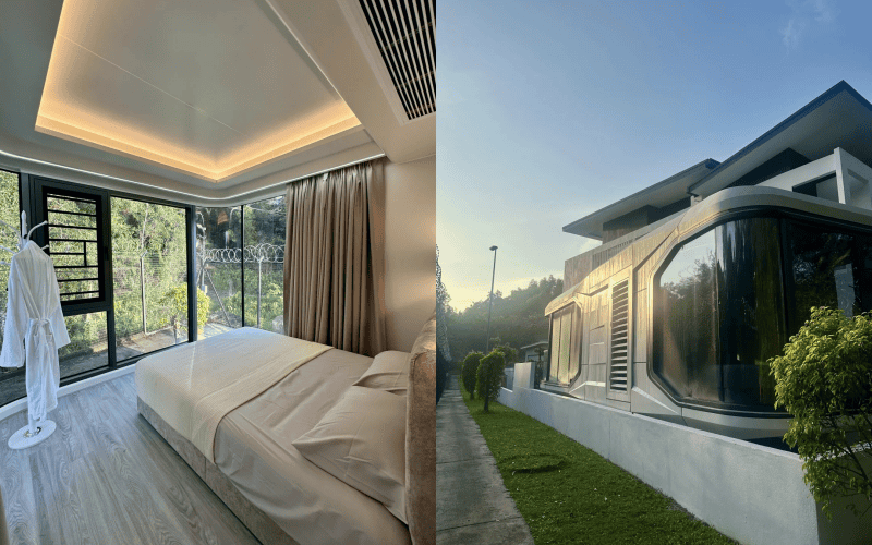 Bedroom inside a capsule house with a bed, a robe on a stand, large windows overlooking greenery.