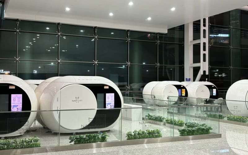 Row of modern - looking capsule houses in an airport setting, each with a screen.