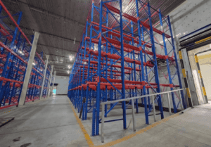 Interior of a Cold Storage Building with blue and red metal shelving units, ready for storing goods, under a metallic ceiling.