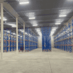 A spacious Cold Storage Building interior featuring rows of blue and red shelving, concrete flooring, and bright overhead lights.