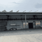 Exterior of a Cold Storage Building with a green roof and metal doors, some storage materials stacked outside.