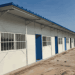 A single-story prefabricated container house row with blue doors and windows, covered by a corrugated roof, placed in an open area.