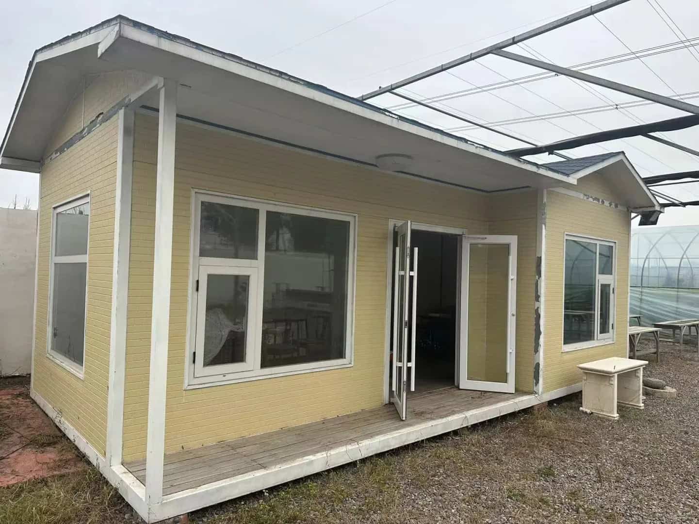 A yellow Container Housing unit with a small porch, windows, and open - doors, set on a gravel surface.