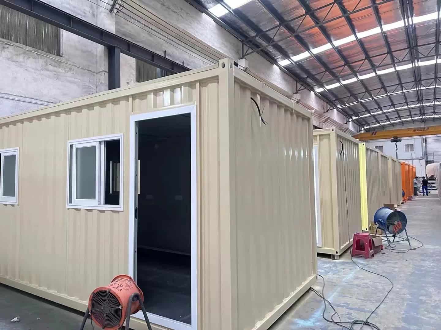 Tan - colored Container Housing units in a factory setting, each with windows and one with an open door.