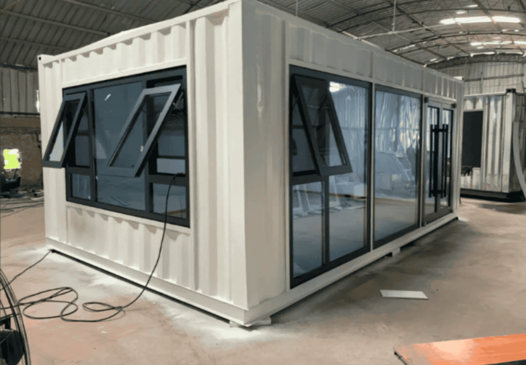 A prefabricated white container office with large glass windows and modern design, displayed inside an industrial facility.