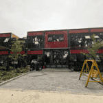 A two-story red and black container office building with greenery around, showcasing modular design and eco-friendly outdoor integration.