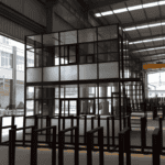 A two-story modular glass structure under construction inside a factory, showcasing a modern and transparent design.