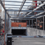 Prefab steel garage framing under construction near a building entrance.