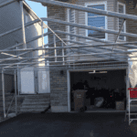 A compact prefab steel garage attached to a brick walled house.