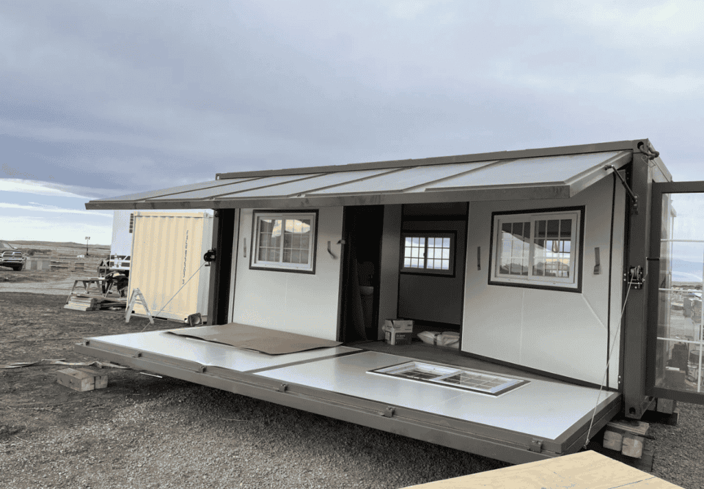 An expandable container house with a foldable platform and awning, showcasing a modern design in an outdoor environment.