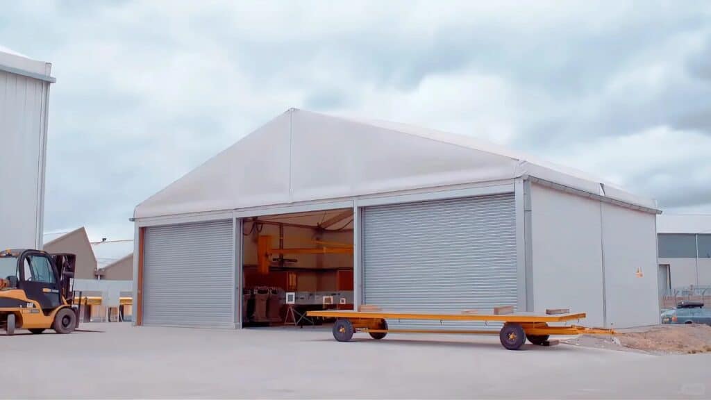 A large farm equipment shed with roll - up doors, a forklift outside, and some equipment visible inside under a cloudy sky.