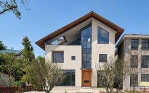 Modern house with a gable roof, large windows, and a wooden door, surrounded by greenery.