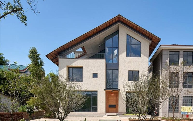 Modern house with a gable roof, large windows, and a wooden door, surrounded by greenery.