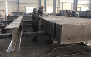 Workers fabricating H beams in a steel structure factory setting.