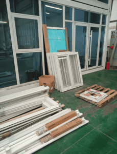 Various window and door frames arranged inside a workshop, featuring aluminum and glass materials.