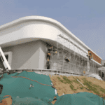 Workers installing facade panels on a light steel building under construction, featuring smooth curves and a minimalist design.