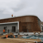 A light steel building under construction with workers and materials on-site, showcasing a unique combination of wood and steel elements.