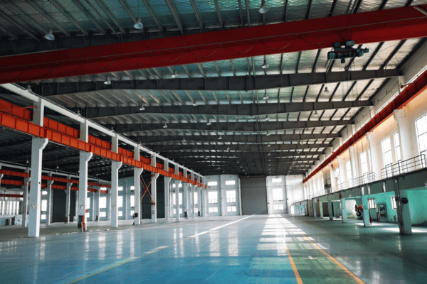 A spacious logistics warehouse with steel beams, overhead cranes, and an open layout.