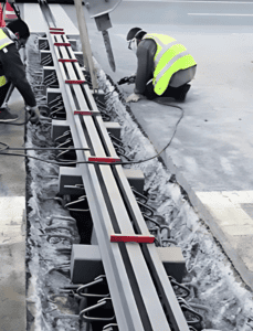 Construction workers installing metal roof expansion joints with visible cables and safety equipment.