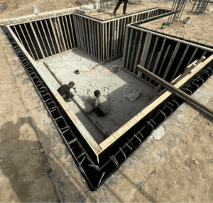 Zwei Arbeiter montieren das Gerüst für einen Keller und legen Holzrahmen als Fundament für eine modulare Struktur.