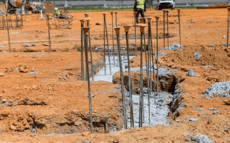 Construction site showcasing a pile foundation with steel reinforcements extending above ground and trenches filled with concrete.