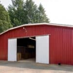 A red pole barn tractor shed with open white doors, surrounded by trees, and some items visible inside.