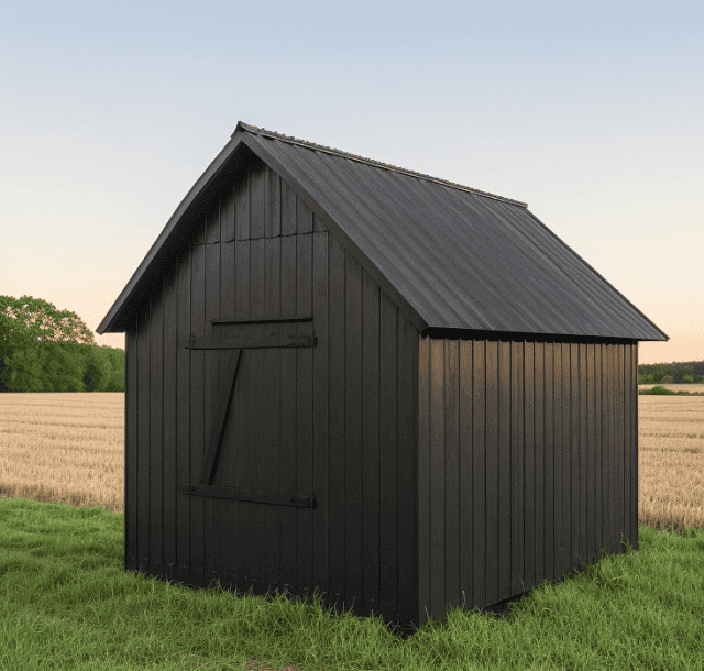 A small black-painted metal barn in a field, featuring a pitched roof and a sliding barn-style door.