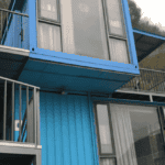 Bright blue modular container structure with glass doors, windows, and balconies, showcasing a modern and stacked architectural design.