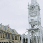 A completed white Prefab Steel Church Building with ornate steelwork, a prominent clock tower, and adjacent historic-looking buildings.