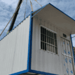 Compact white container home being lifted by a crane, emphasizing portability and efficient installation for temporary housing.