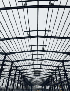 Interior framework of a steel structure building showing symmetrical roof trusses and vertical columns extending into the distance.