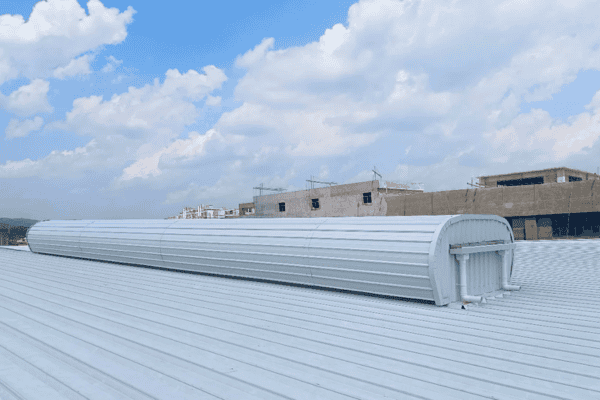 A curved white rooftop structure with ventilation units, set against a backdrop of clouds and nearby buildings.