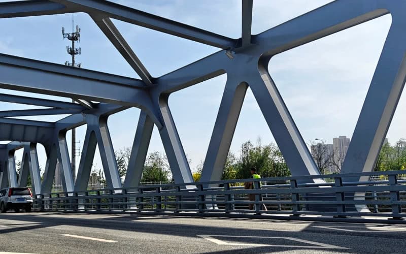 Close - up of a steel truss bridge's framework with cars on the road.