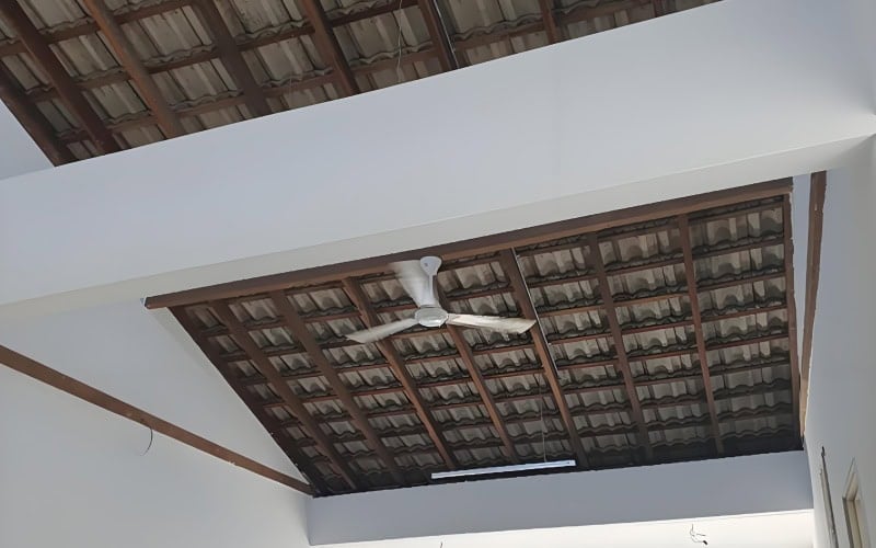 Interior view with a wooden roof truss supporting tiled roofing and a ceiling fan.