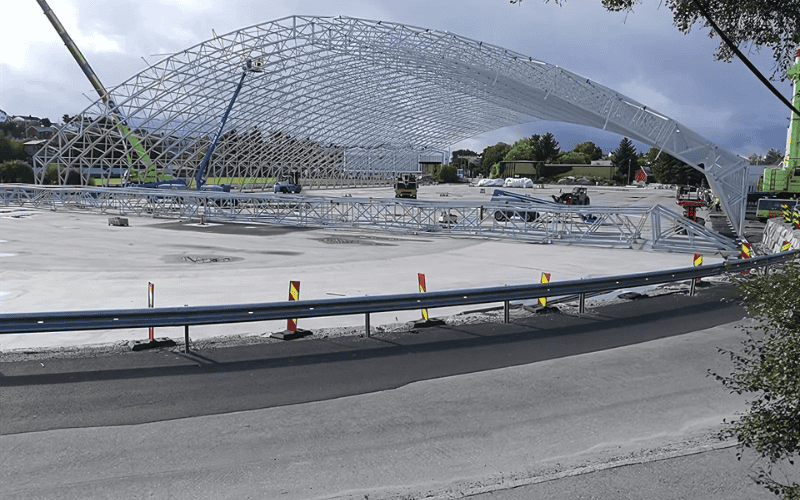 Under construction steel framework for a skating rink, with cranes and barriers in place.