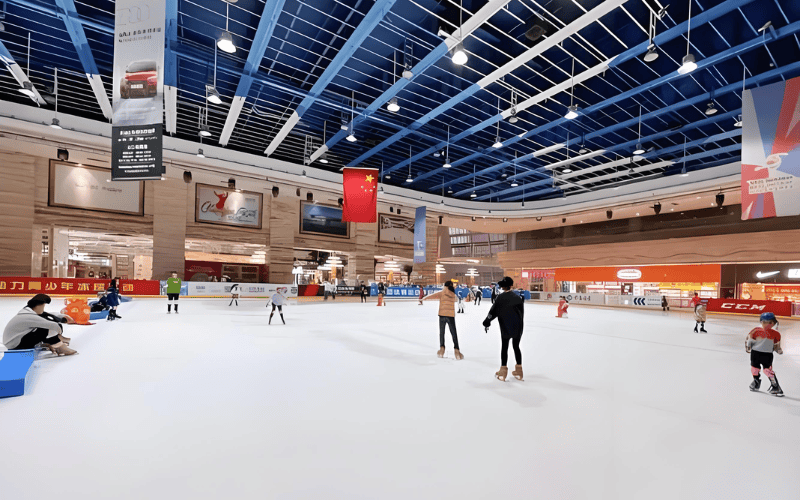 Steel framed skating rink in a shopping mall, with banners hanging from the blue ceiling and skaters on the ice.