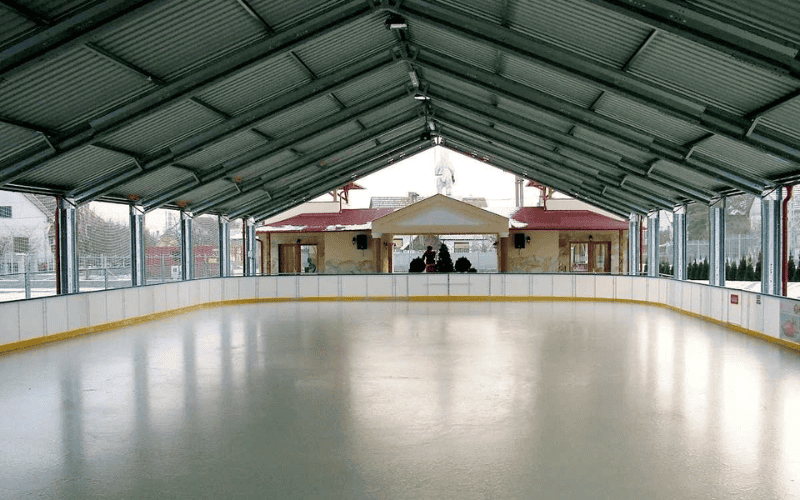 Steel framed skating rink in a shopping mall, with banners hanging from the blue ceiling and skaters on the ice.