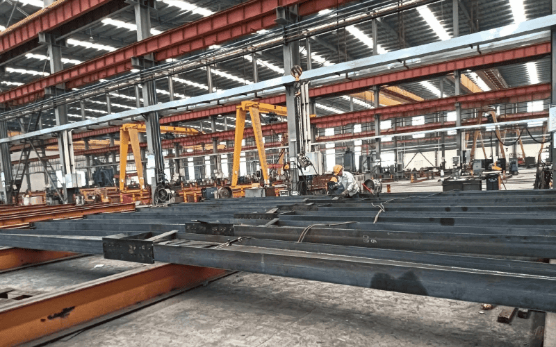 Steel structure beams in a factory setting, ready for fabrication or assembly.