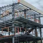 Exterior view of a partially completed Steel Structure Multi-Storey Building with a corrugated metal roof, orange framework accents, and open floor levels.