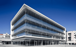 Modern steel structure office design with sleek lines, large glass - paned windows, and multiple floors under a clear blue sky.