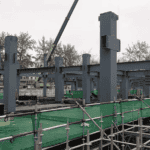 Steel framework of a Steel Structure School Building under construction, featuring green safety netting and large structural beams and columns.