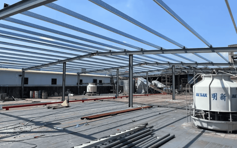 Steel Building Construction - A large steel-framed structure under construction with horizontal beams spanning across an open workspace.