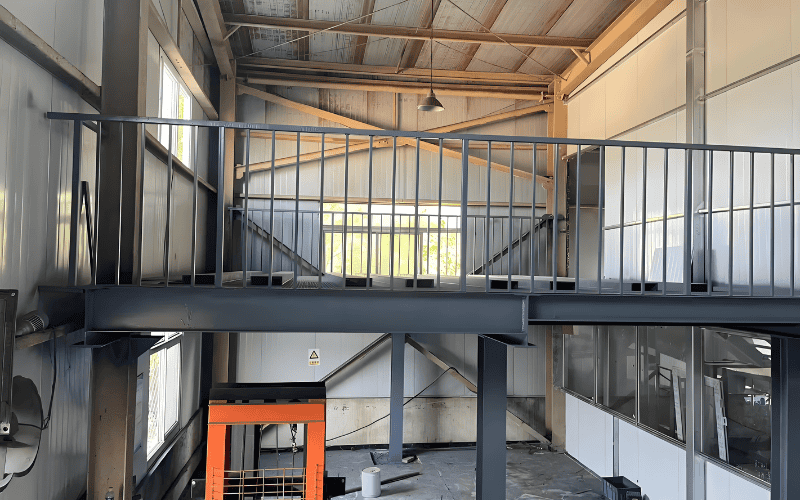 Steel structure platform inside a warehouse, featuring metal railings and an overhead light.