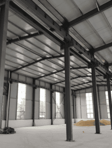 Spacious interior of a steel structure workshop with high ceilings, vertical steel columns, and natural light coming through large windows.